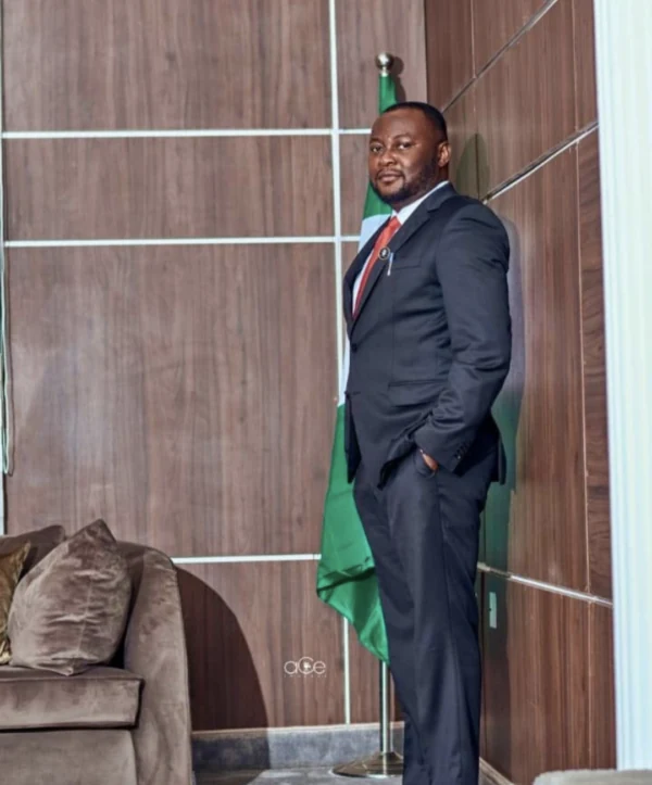 Pelumi Olajengbesi in a dark suit standing beside a Nigerian flag